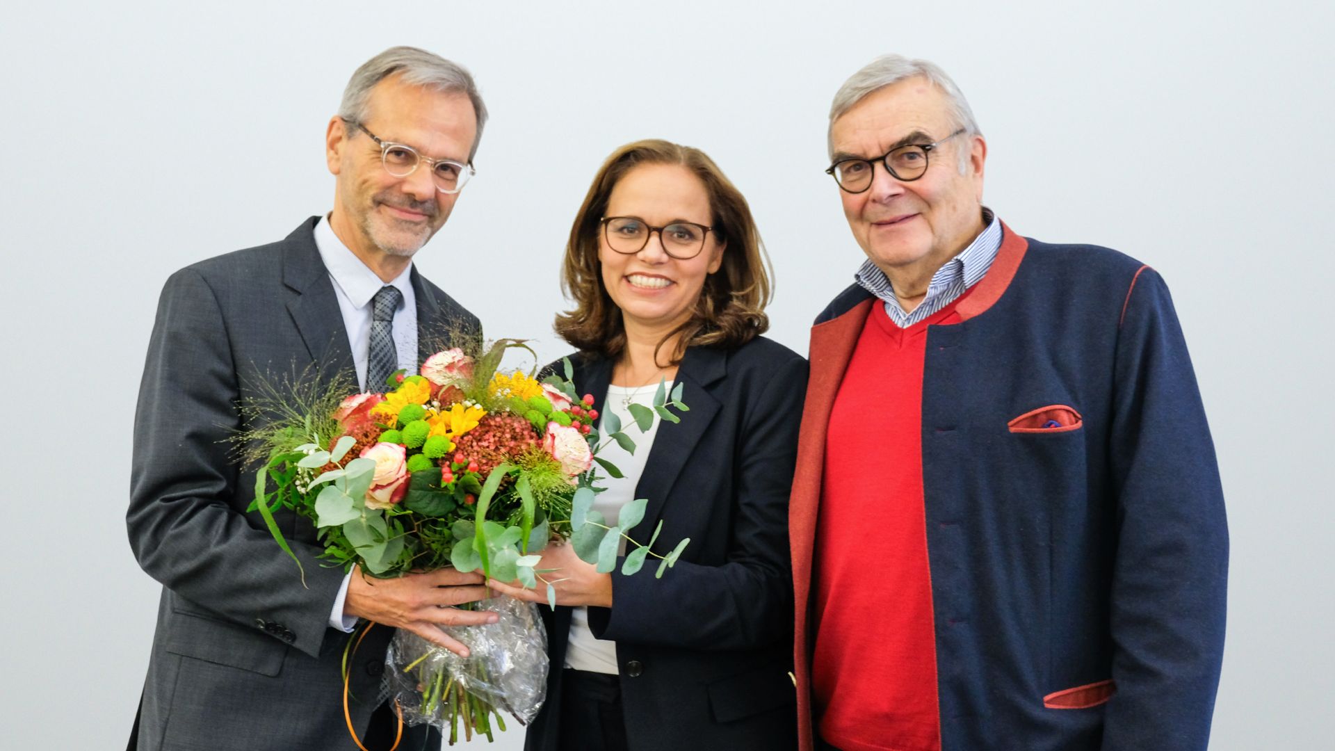 Eine Frau und zwei Männer stehen nebeneinander und schauen in die Kamera. Die Geschäftsführerin überreicht dem neuen Ärztlichen Direktor einen Blumenstrauß.